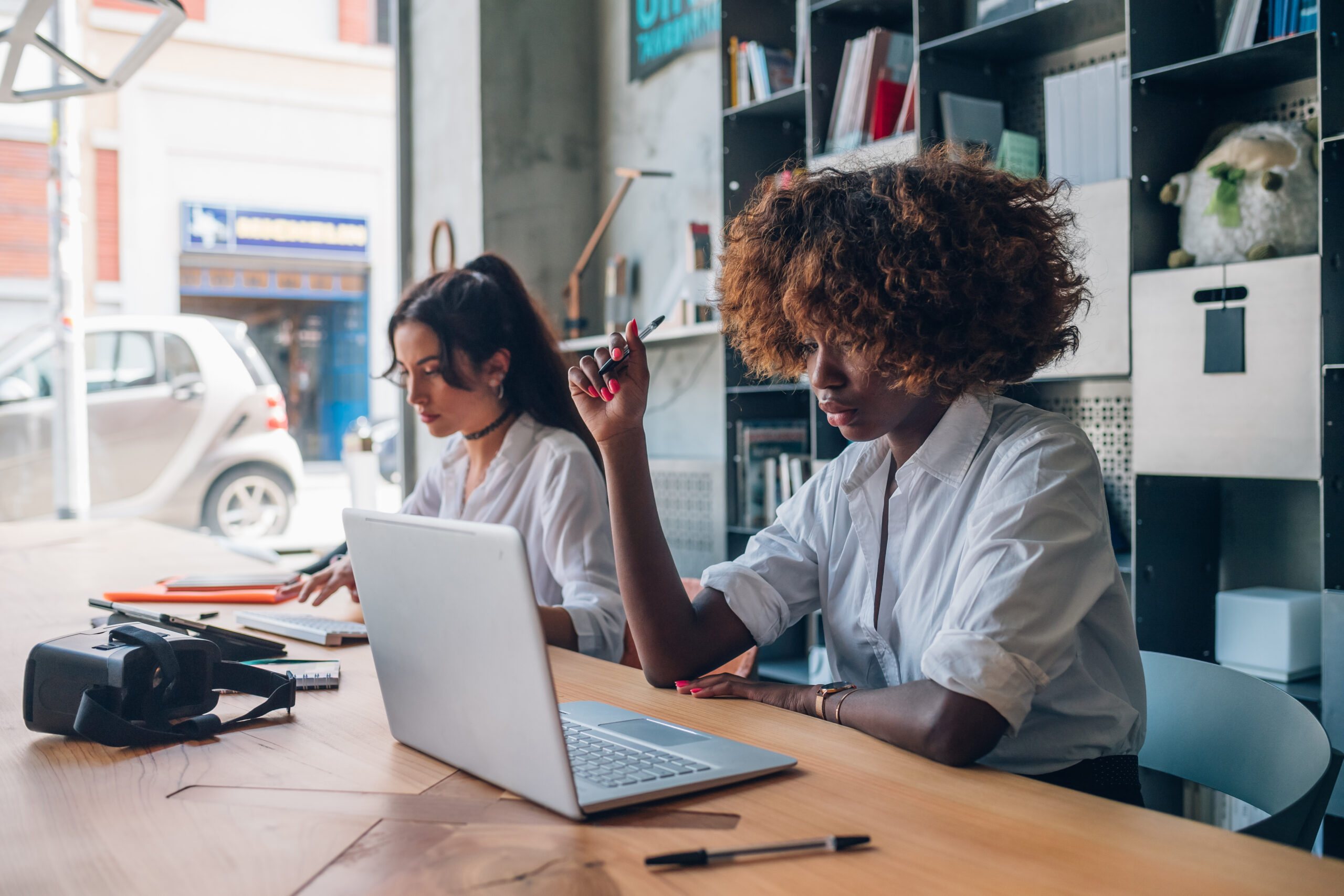 two young multiracial women writing working with digital device modern coworking space scaled